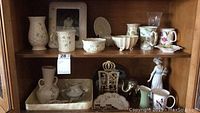 Wooden cabinet shelf displaying Belleek vases, mug, bowls, Lladro figurine, Lenox pitcher, additional items