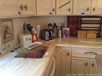 Full kitchen counter setup showing multiple kitchen items and some utensils with toaster, copper pitcher, glass vase, spice racks, napkin holders and paper towel holder.