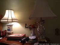 Three table lamps on wooden surfaces including a tall clear glass diamond-pattern base lamp and a rectangular white base lamp with shade, a ceramic lamp with white shade, and a white ceramic vase with faux flowers.