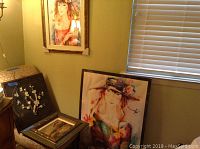 Photo showing several pieces of wall art: two framed pastel-tone paintings of women with floral hats, one floral Asian art piece, and one framed landscape oil painting leaning on a chair.