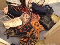 Photo showing multiple assorted handbags and travel bags in various colors and materials spread on carpeted floor.
