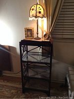 Full view of the wood frame shelf with 2 glass shelves and items on top including lamp, clock, picture frame, and magnifying glass