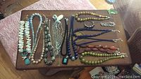 Overview of 12 necklaces, bracelets, and pendants laid out on wooden surface.