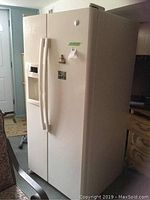 Front and side view of the white GE side by side refrigerator freezer in a room, showing the handles and overall size.