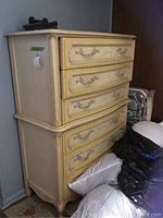 Front and side view of the vintage Stanley chest of drawers showing six drawers, distressed off-white paint with yellow accents, metal handles, and curved legs.