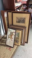Photo of stacked framed vintage prints and artwork leaning against a shelf, showing varied sizes and frame styles