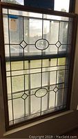 Leaded glass window panel with oval and geometric designs in a wooden frame, seen from the front with natural light through it.