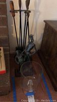 Fireplace tool set with wooden handles on metal stand next to wall and shelf