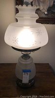 Full view of the table lamp showing frosted glass body and shade with light on inside.