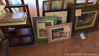 Framed wall art and pictures leaning against wall and carpet showing some stains on one frame