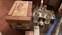 Photo showing decorative box with painted floral and fruit artwork and four angel figurines placed on top and around it.