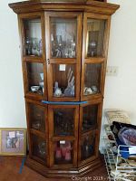 Front view of the closed wooden curio cabinet with glass shelves showing various glassware inside, no contents included in sale.