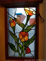 Stained glass window with orange and yellow flowers on green stems and textured clear glass background