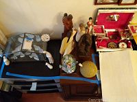 Overview of various figurines, jewelry box with jewelry inside, and candy dish on black table surface