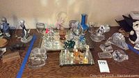 Photo of a collection of glass figurines, mini perfume bottles, small animal figurines, and mini vases displayed on a mirrored tray and wooden surface.