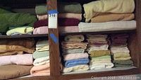 Shelves filled with folded towels in various pastel and earth tones, including greens, yellows, pinks, blues, and creams, stacked neatly showing a range of sizes.