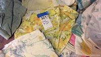 Assorted vintage bedding and sheets showing yellow floral patterned sheet, green and white floral sheet, blue and cream sheet, and gray solid bedding.