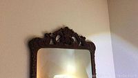 Front view of the ornate hand carved wood frame mirror against a wall.