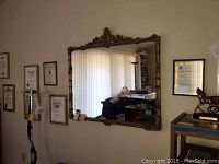 Front view of large gilt framed wall mirror in a living area, showing clear reflective surface and detailed frame.