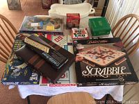 Photo of nine table games arranged on a dining table including Deluxe Edition Scrabble, Sudoku, Cribbage, Trivial Pursuit, Backgammon, Monopoly, Wheel of Fortune, and more