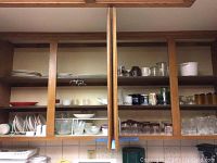 Wide shot of wooden shelves with various kitchenware items including plates, bowls, mugs, and glasses arranged in an orderly manner