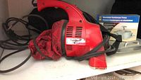 Red Dirt Devil vacuum cleaner with red fabric dust bag and electrical cord coiled, visible controls on top, angled nozzle.