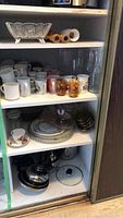Overview of four shelves showing mugs, glass bowls, plates, and dishes