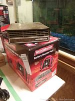 Rectangular compact MotorMaster 12V car heater with vent grille, placed on top of the MotorMaster battery booster pack box.
