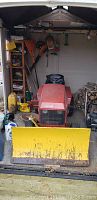 Front view of red Troy-Bilt tractor with yellow snow plow attached, parked in shed