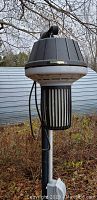 Outdoor photo showing the Flowtron bug zapper hanging on a metal pole with vegetation background.