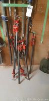 Group of red steel bar clamps of various lengths leaning against pegboard