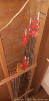 Overview of ten pipe clamps stored vertically in wood rack