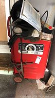 Full view of red Lincoln Electric welder with cables, electrodes and manual on top