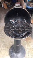 Front view of the black electric BBQ grill with open lid, showing interior grill grate, heating coil, and temperature control dial with power cord on top.