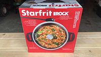 Front of the box of the Starfrit The Rock electric multi-pot with image of wok filled with cooked vegetables and shrimp.