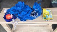 Blue fabric drift sock laid out with attached orange buoy and white rope, placed on a wooden table, with a small blue storage bag and informational packaging.