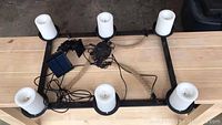 Top-down view of rectangular black metal light fixture with six white candle-style lights and coiled wiring leading to solar panel.
