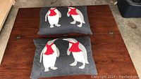 Two square pillows lying on a wooden surface featuring penguins with red scarves on dark gray fabric.