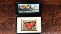 Two framed original paintings - larger landscape by Jan Russell above, smaller tomato still life by WM Mitchell below on a wooden surface