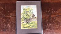 Full view of the framed watercolor painting by Celia Sage showing the rustic house, tree, and surrounding field.
