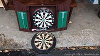 Dart board inside a wooden cabinet with two green scoring panels on either side, placed on the ground outside.