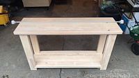 Front angle of unfinished pine console table with metal extending curtain rod resting on top.