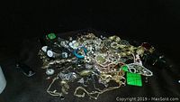 Full view of assorted jewelry pile including watches, bracelets, necklaces, and brooches spread out on a dark cloth background.