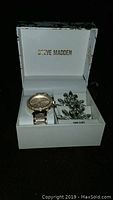 Steve Madden watch and earrings set in branded white gift box shown from front angle.