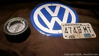 Photo of Volkswagen emblem sign, Goodyear Eagle tire ashtray, and Georgia license plate visible from above on fabric surface