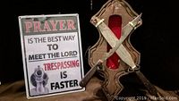 Full view showing the antique style blade crossed on a wooden cross-shaped display with red fabric lining next to a printed sign.