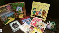 Photo showing a collection of Wizard of Oz themed books, VHS tapes, DVDs, diary, and record album arranged on a dark cloth surface.