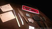 Wide view of all items showing knives, ration books, playing cards, sheath, and first aid tin.