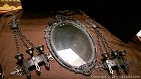 Full view of the cast iron mirror and candle holder set on a dark fabric background.