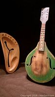 Image showing the detached neck and body of the handmade wooden string instrument, with body showing two f-holes and faded green paint